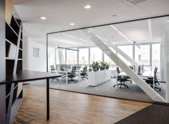 Heller, moderner Bürobereich mit Glaswänden, Schreibtischen und großen Fenstern, die viel Tageslicht hereinlassen.