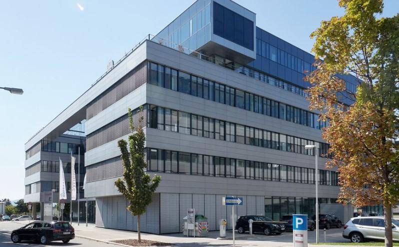 Ansicht des modernen Bürokomplexes von der Straßenseite, mit mehreren Etagen, großen Fenstern und angrenzenden Parkplätzen.