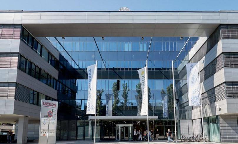 Eingangsbereich eines modernen Bürogebäudes mit beeindruckender Glasfassade und Drehkarusselltür.