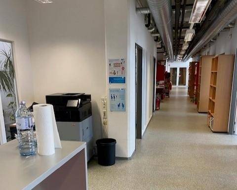 Langer Flur in einem Bürogebäude mit Druckerstation und Regalen, gut beleuchtet und funktional.
