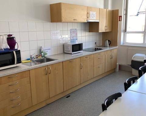 Funktionale Küche mit Holzschränken, Spüle, Mikrowelle und Wasserdispenser, ideal für Mitarbeiter.