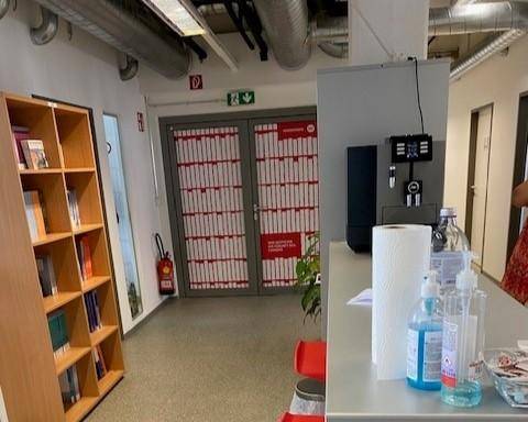 Büroflur mit Kaffeemaschine, Bücherregal und Brandschutzvorrichtungen, funktional und gut ausgestattet.