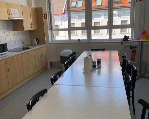Geräumige Gemeinschaftsküche mit langer Tafel, Holzschränken und großem Fenster mit Stadtblick.