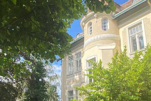 Historische Fassade eines eleganten Gebäudes, umgeben von üppigem Grün und Bäumen.