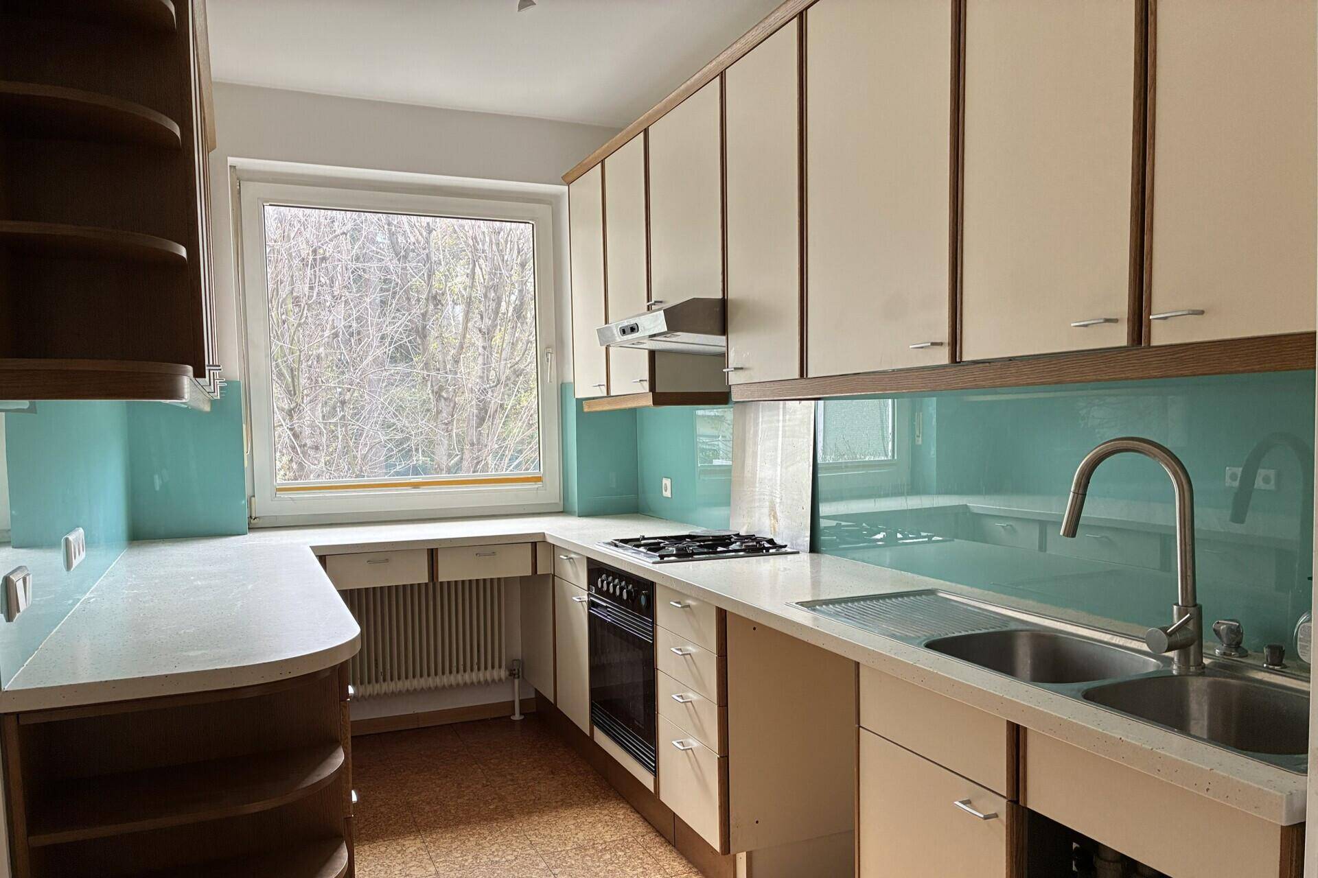 Funktionale Küche mit beigen Schränken, Gasherd und Fenster mit Blick ins Grüne.