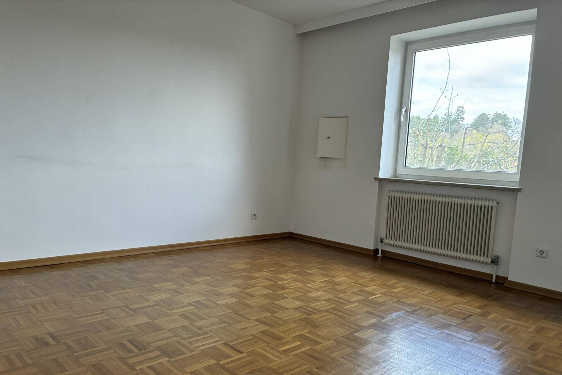 Helles Schlafzimmer mit Parkettboden und großem Fenster, bereit zur individuellen Gestaltung.