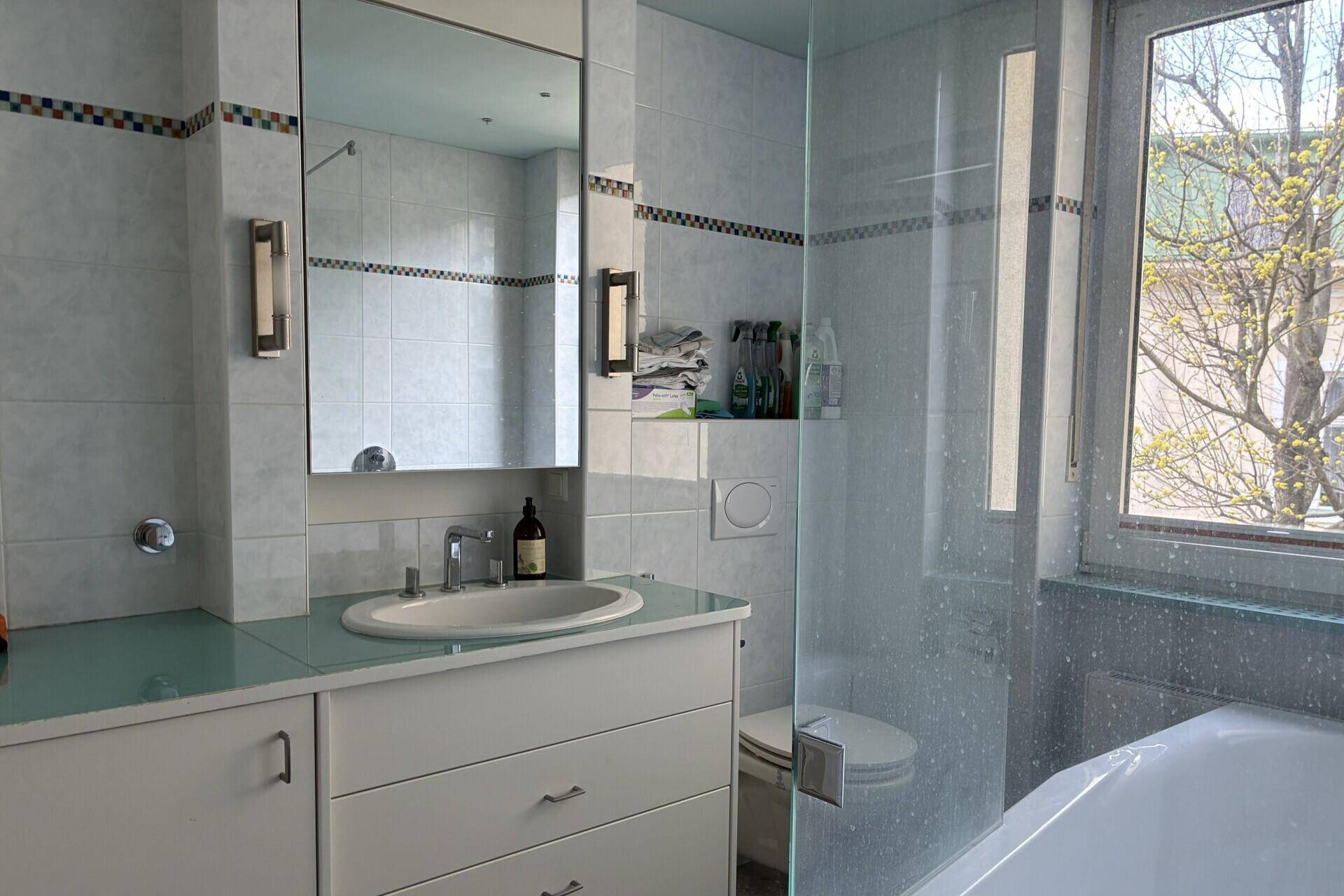 Modernes Badezimmer mit Fliesen, Waschtisch, Dusche und Fenster für Tageslicht.