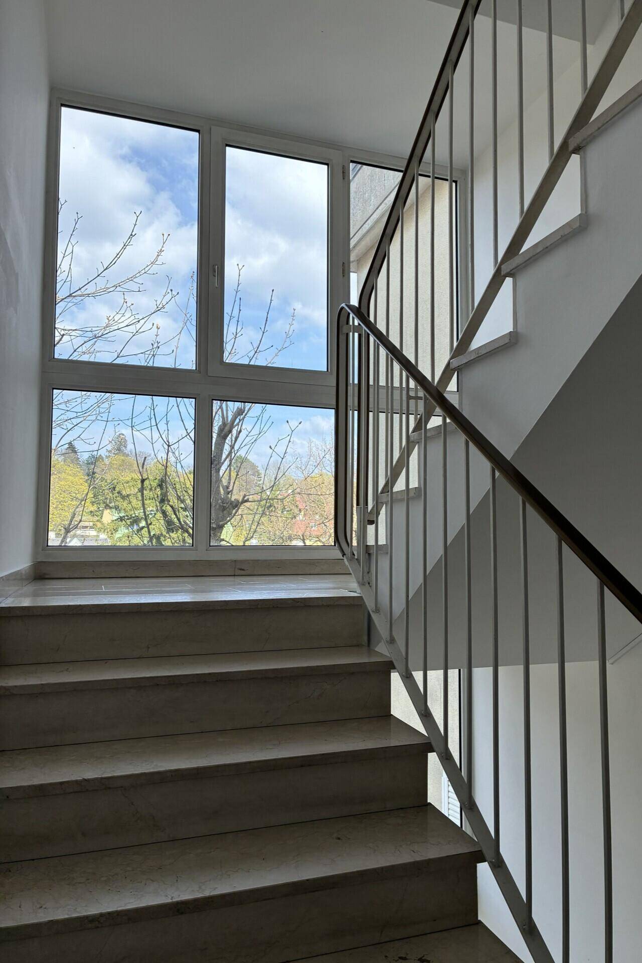 Treppenhaus mit Marmorstufen und großen Fenstern, die viel Licht spenden.