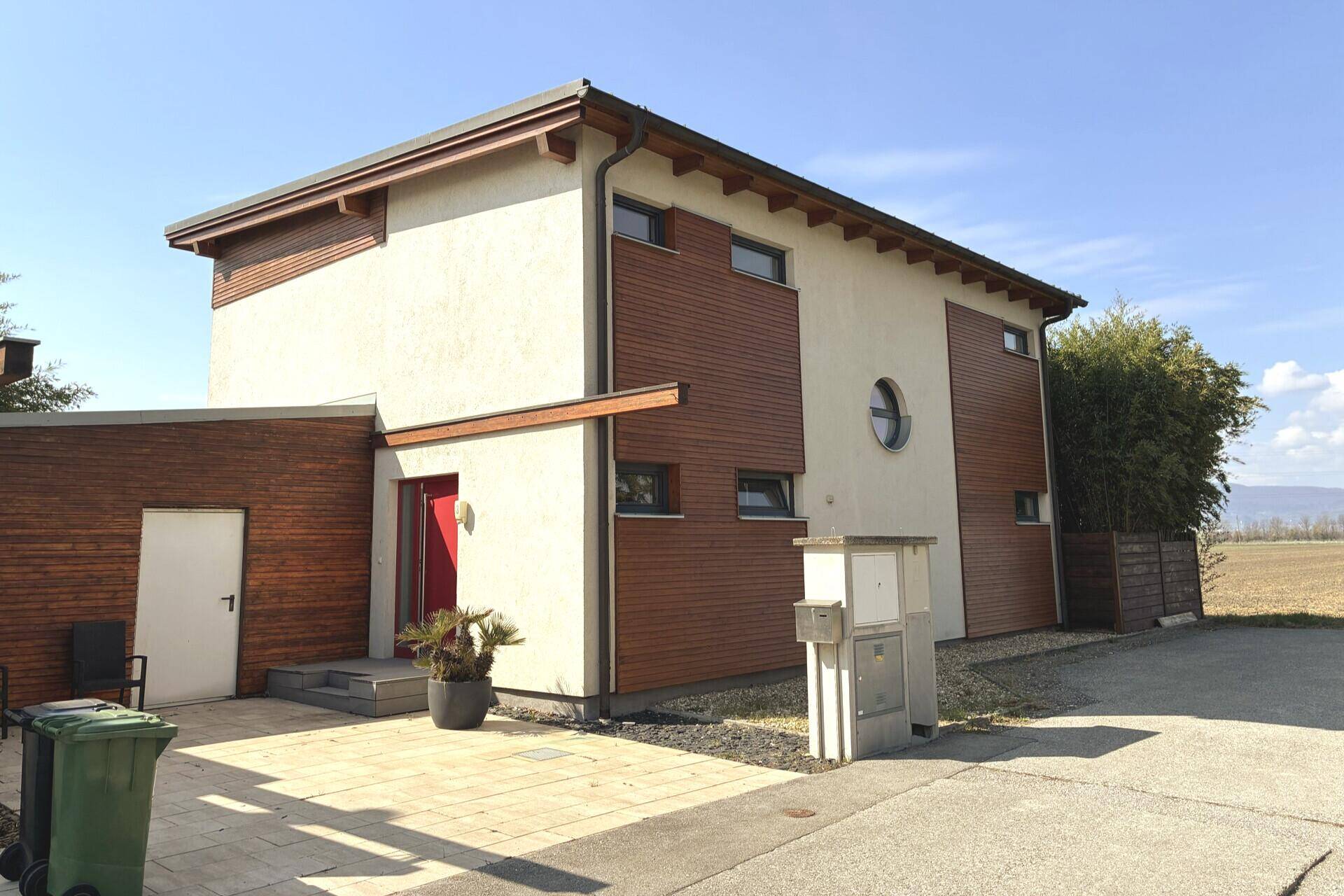 Moderne Hausfassade mit Holzverkleidung, hellen Putzflächen und runden Fenstern.