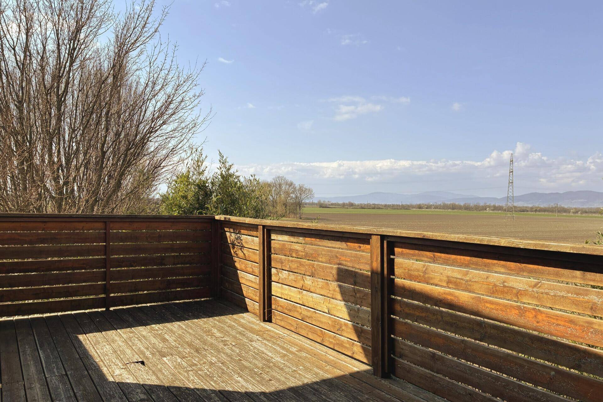 Geräumige Holzterrasse mit weitem Blick über die umliegende Landschaft und Felder.