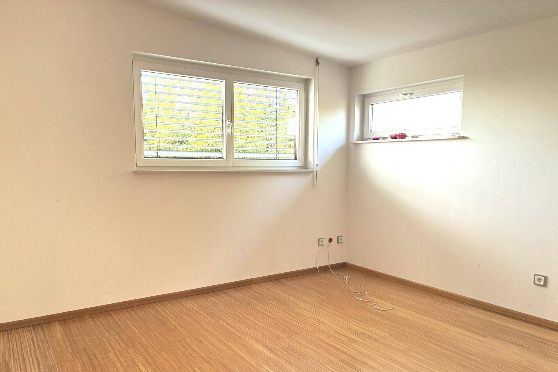Leeres Zimmer mit Holzfußboden und zwei Fenstern, ideal als Schlaf- oder Arbeitszimmer.