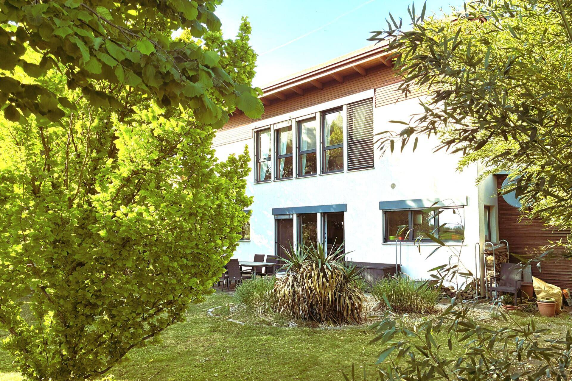 Rückansicht des Hauses mit gepflegtem Garten, Terrasse und üppiger Bepflanzung.