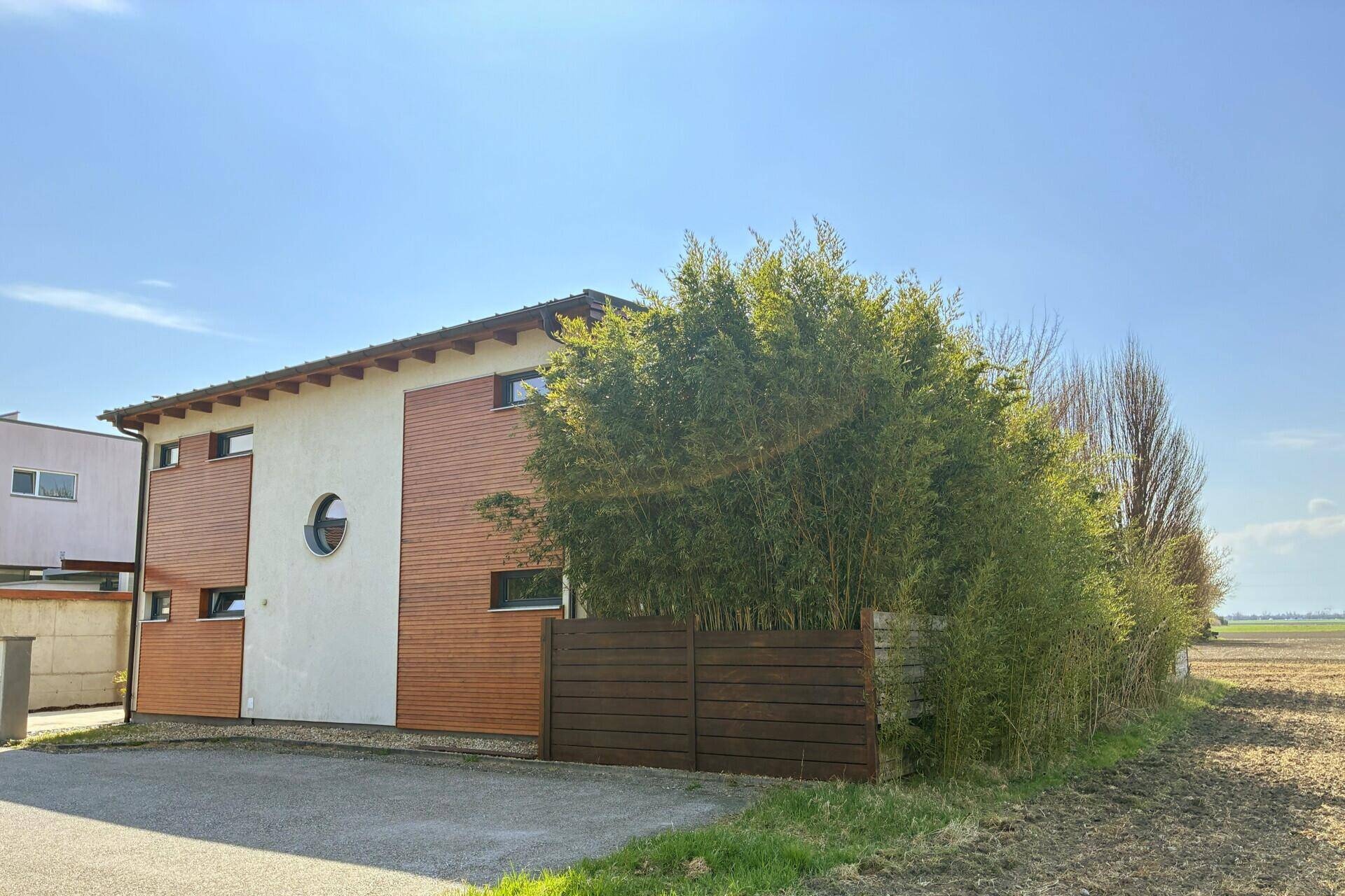 Seitenansicht des modernen Hauses mit Holzverkleidung und umgebender Natur.