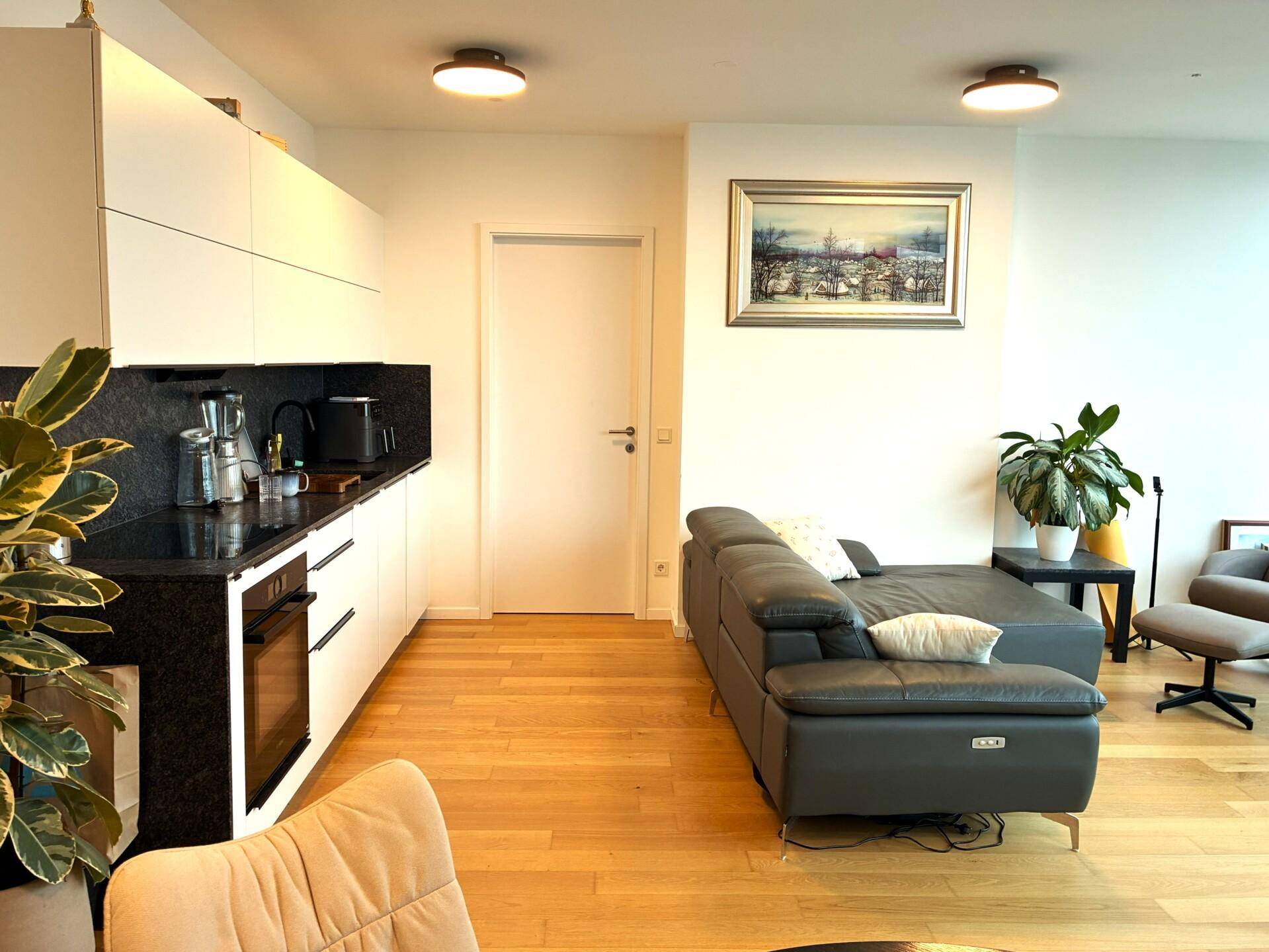 Lichtdurchfluteter Wohnbereich mit integrierter Küche, bequemer Couch und Holzboden.