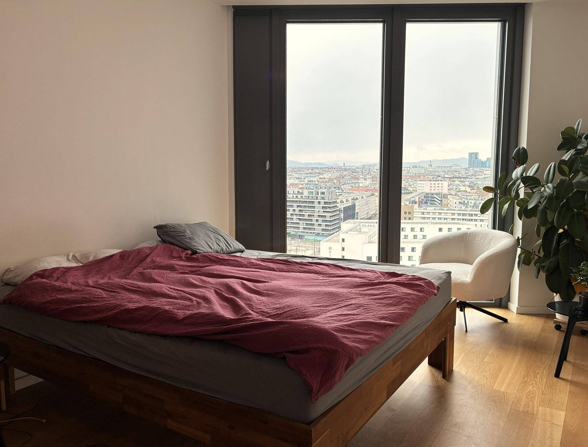 Schlafzimmer mit Holzbett, großen Fenstern und beeindruckendem Stadtblick.
