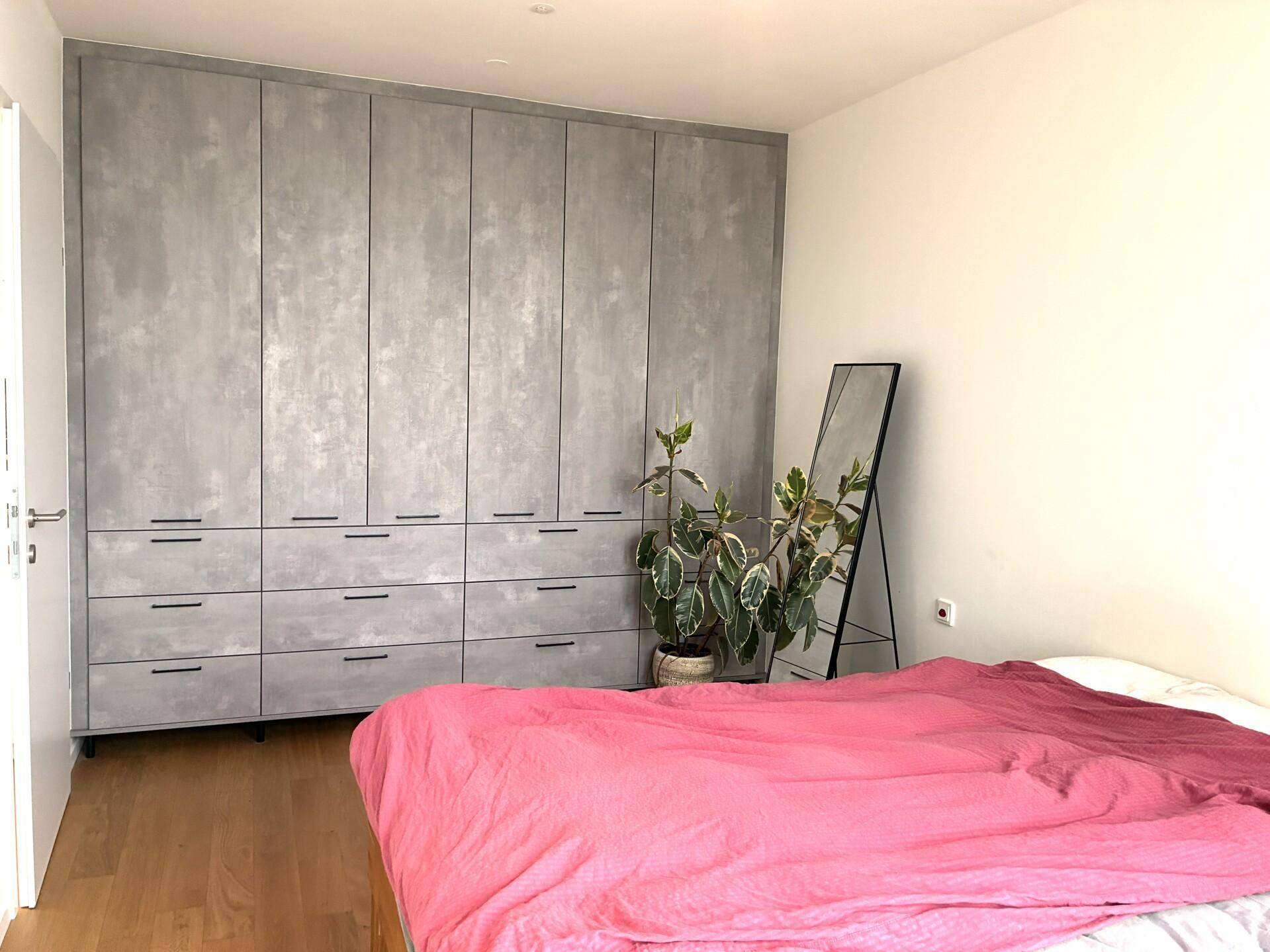 Schlafzimmer mit großem, modernem Einbauschrank in Betonoptik und Holzboden.