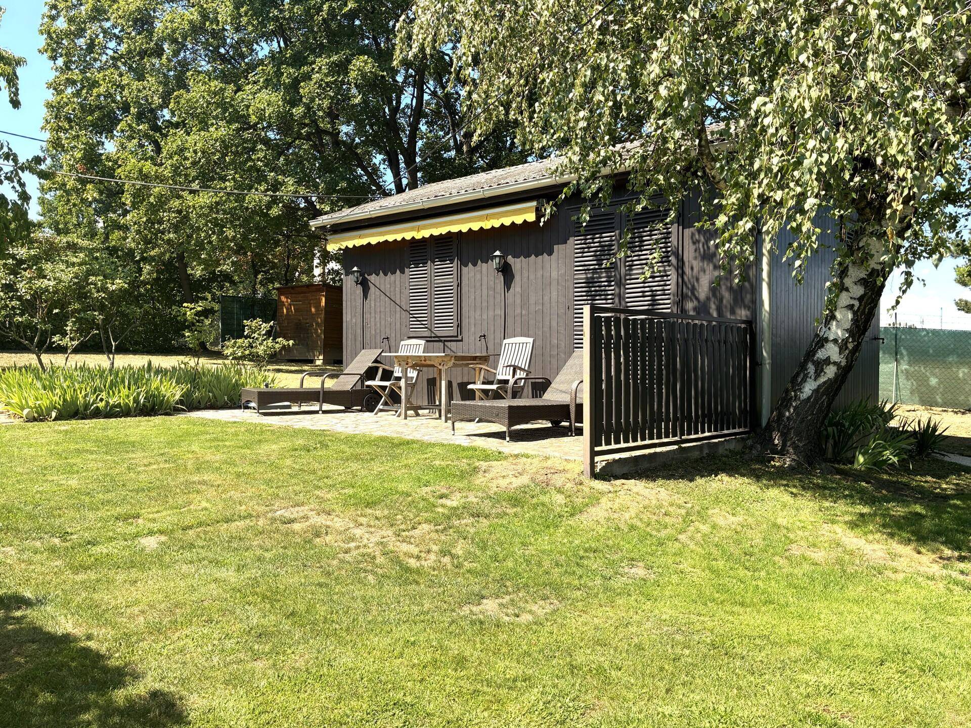 Gemütliche Terrasse mit Gartenmöbeln und Sonnenliegen vor einem dunklen Holzhaus mit Markise.