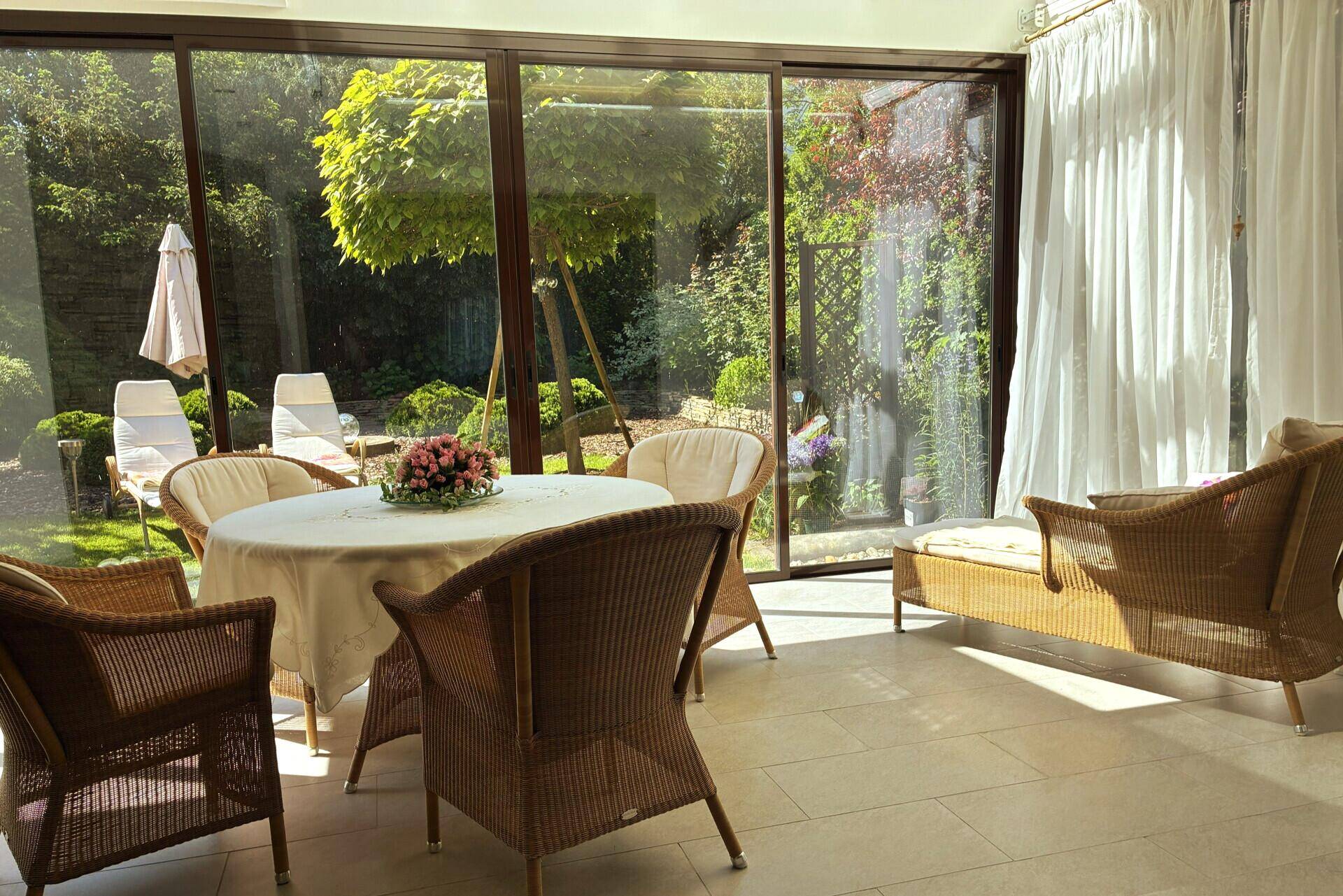 Heller Wintergarten mit Rattanmöbeln und Blick auf den grünen, sonnigen Garten.