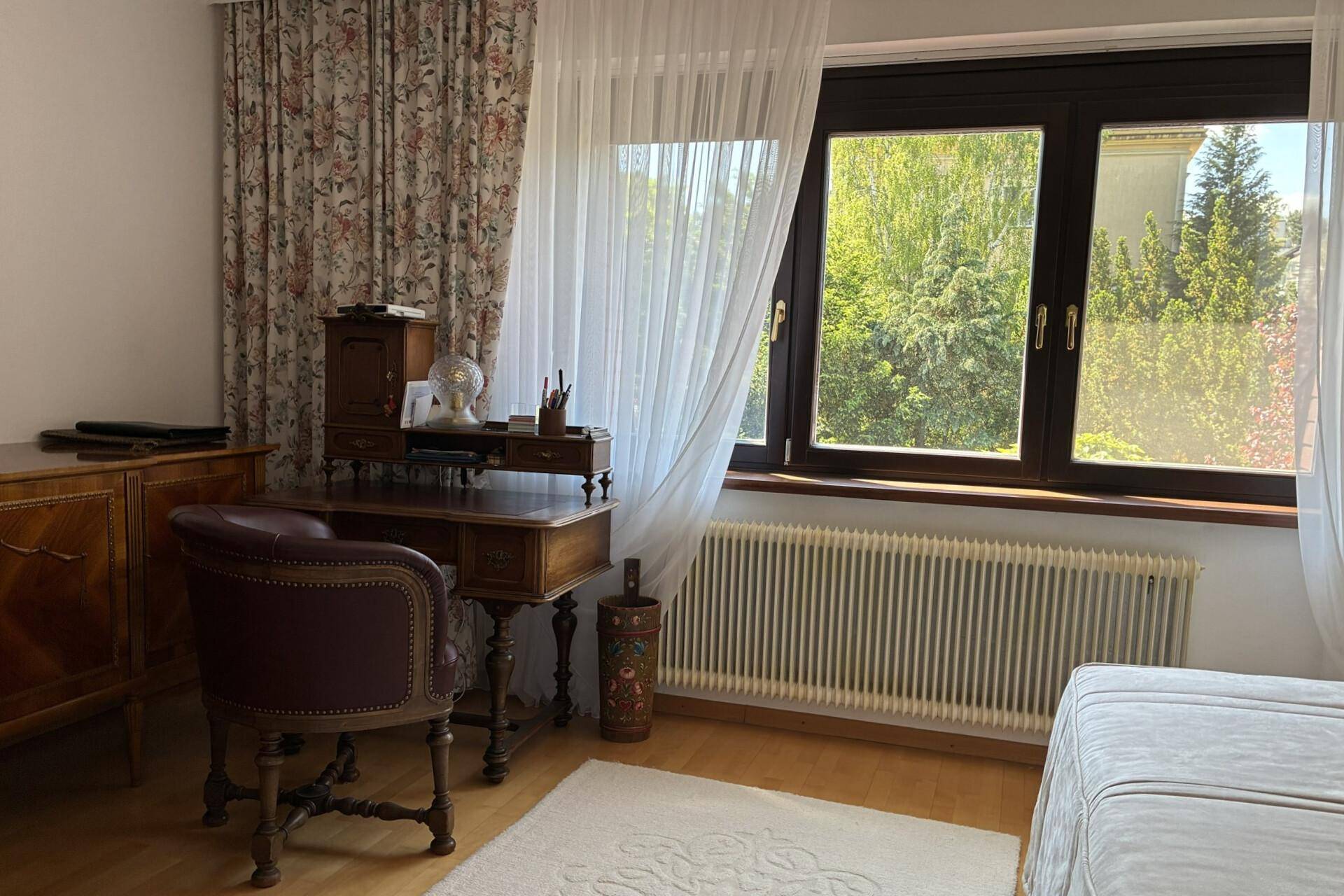 Helles Arbeitszimmer mit klassischem Schreibtisch, Holzmöbeln und Blick ins Grüne.