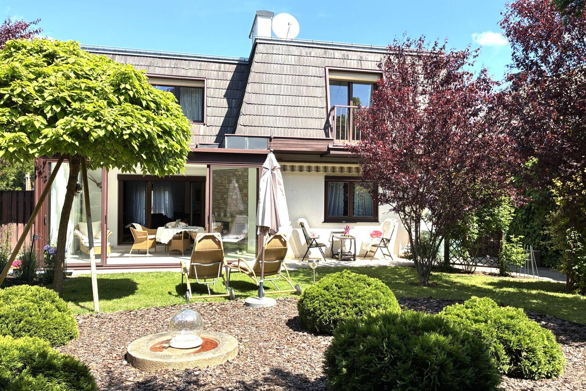 Rückansicht des Hauses mit Terrasse, Wintergarten und weitläufigem, sonnigem Gartenbereich.