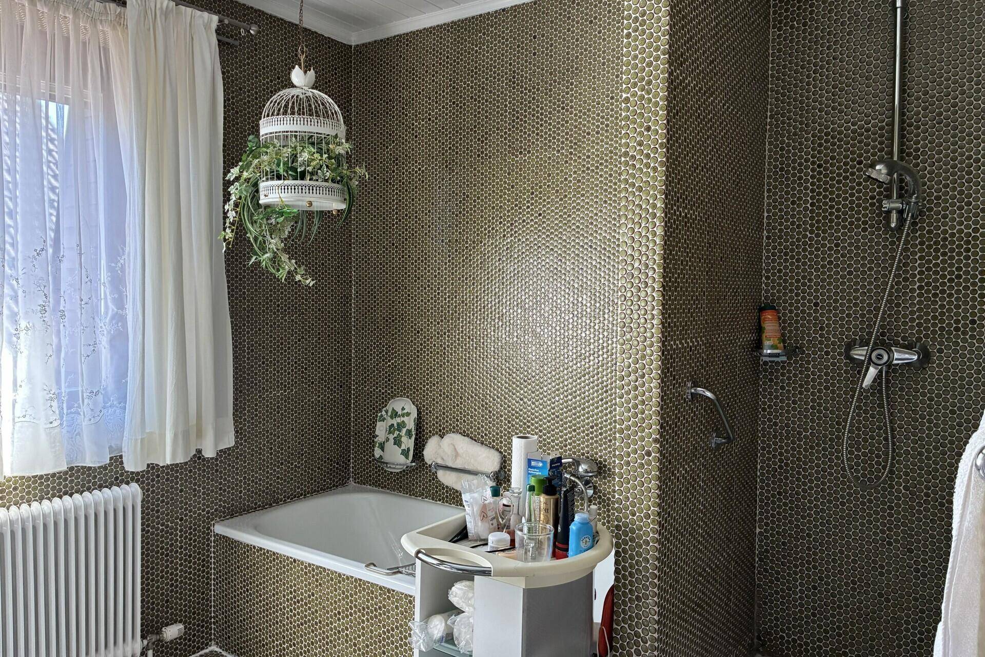 Badezimmer mit Badewanne, Duschbereich und auffälligen Mosaikfliesen in Grüntönen.