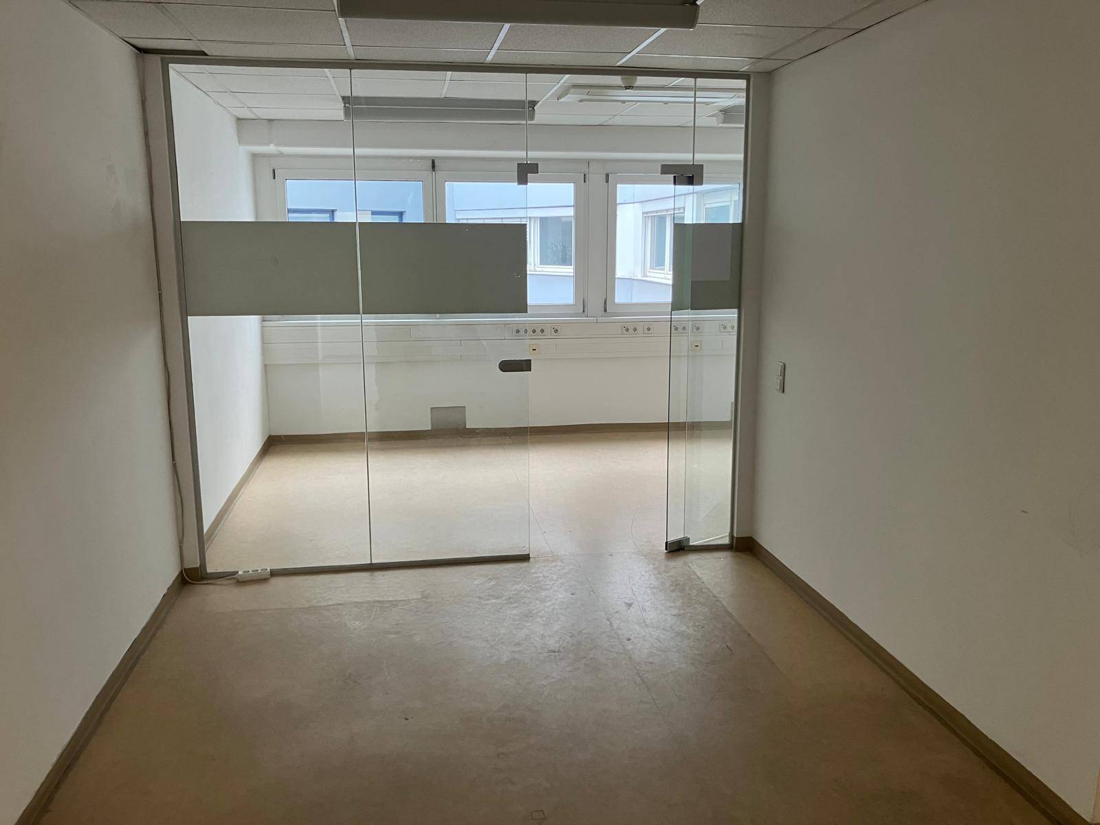 Leerer Büroraum mit großen Glaswänden und Blick auf weitere Büros durch die Fenster.