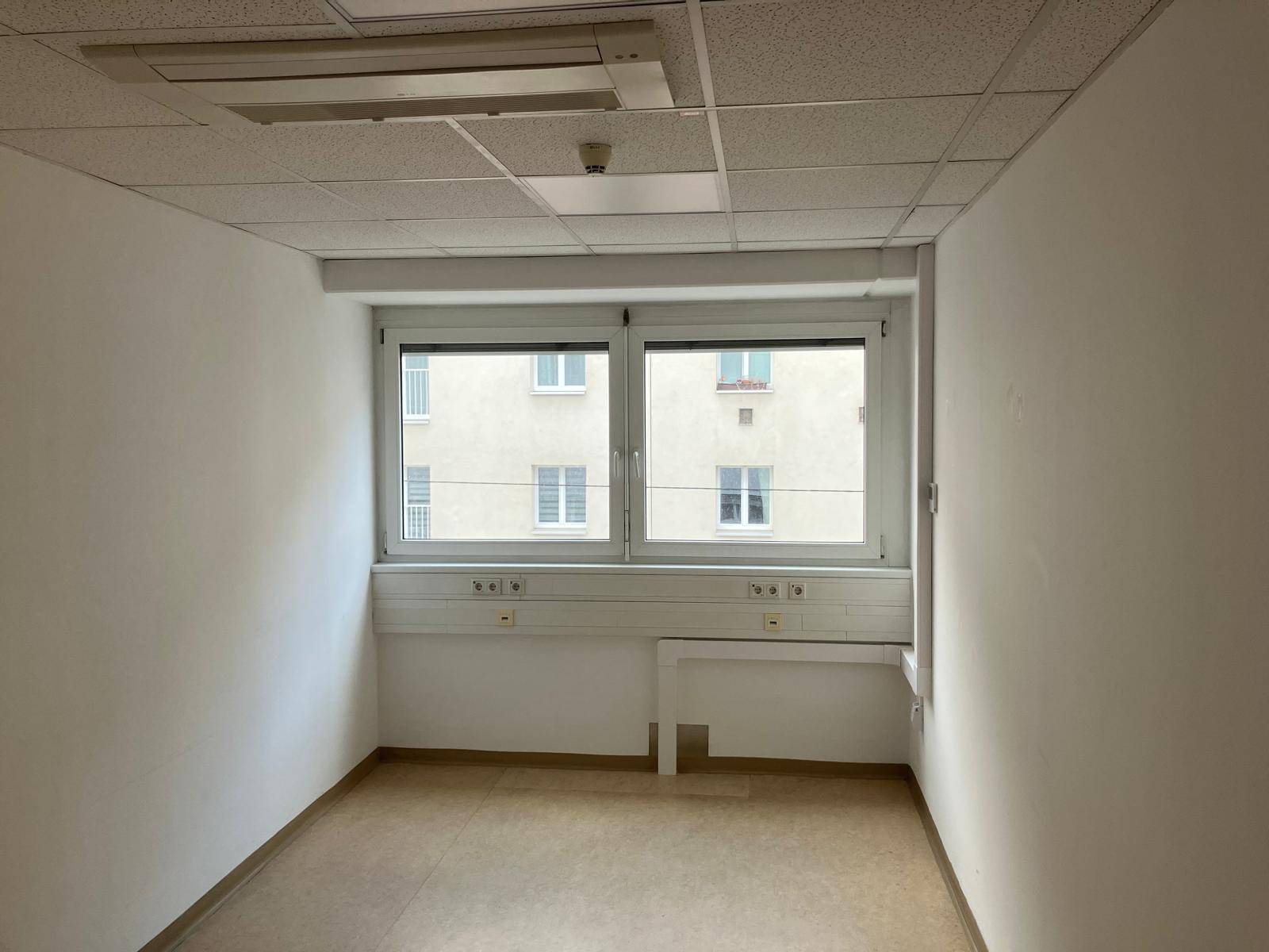 Kleinerer Büroraum mit einem großen Fenster, das viel Tageslicht hereinlässt und Blick auf Gebäude bietet.