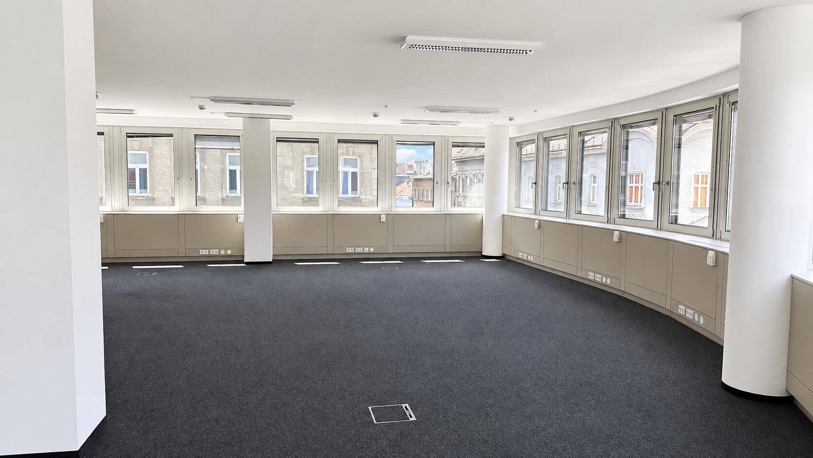 Großes, helles Büro mit Teppichboden und einer Reihe von Fenstern entlang einer gekrümmten Wand.