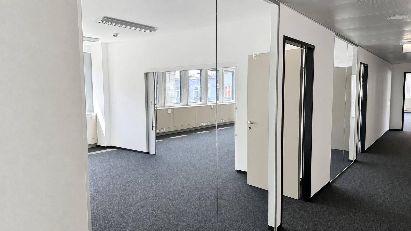 Moderner Bürogang mit Glaswänden, die den Blick in die angrenzenden Büroräume freigeben.