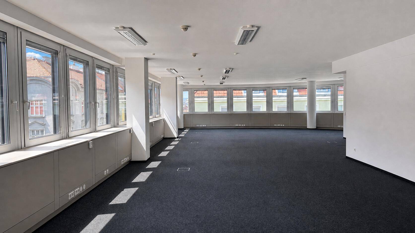 Sehr großes, offenes Büro mit Teppichboden und zahlreichen Fenstern, die viel Tageslicht hereinlassen.