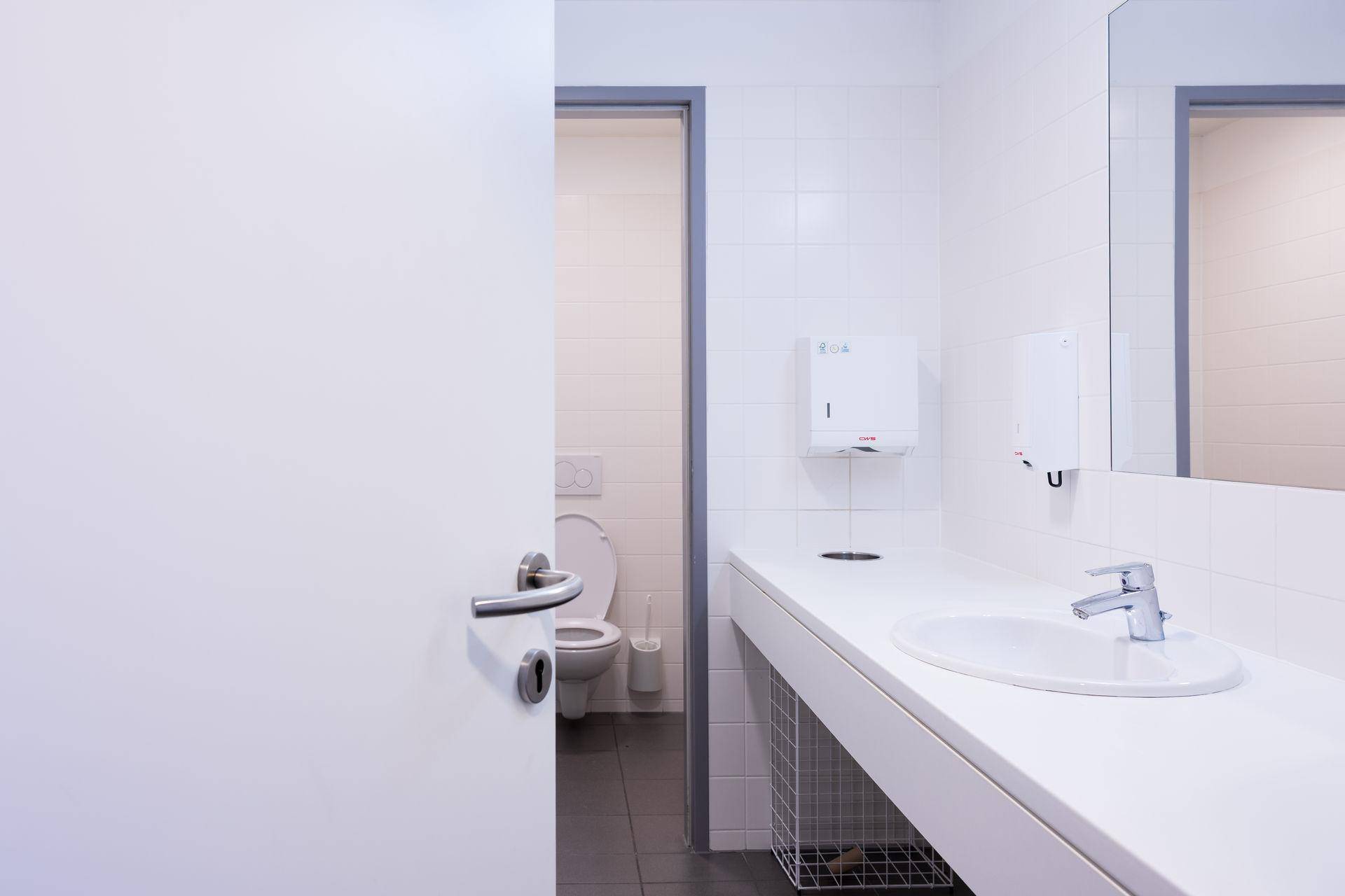 Helles Badezimmer mit Waschbecken, Spiegel und einer Toilette, ausgestattet mit weißen Fliesen.