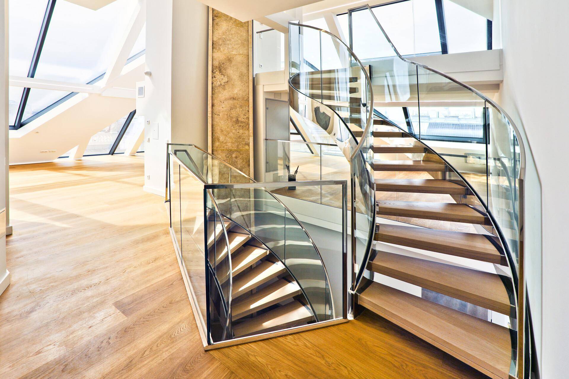 Moderne Wendeltreppe mit Glasgeländer, die den Wohnbereich mit der oberen Etage verbindet.