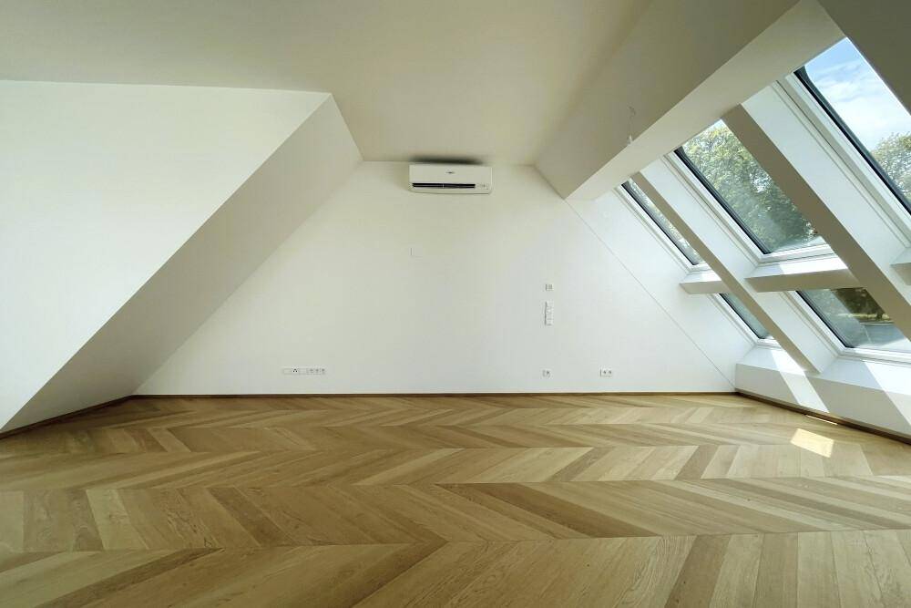 Helles Zimmer mit Dachschrägen, Fischgrätparkett und Klimaanlage unter den Dachfenstern.