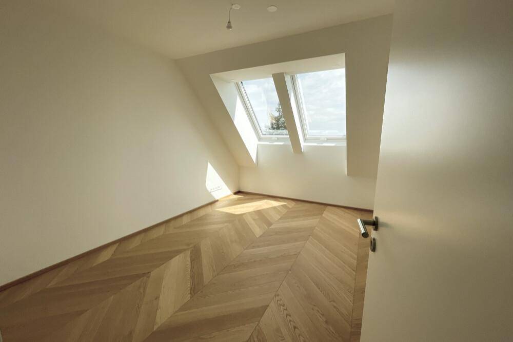 Helles Schlafzimmer mit Fischgrätparkett, Dachschrägen und zwei großen Dachfenstern.