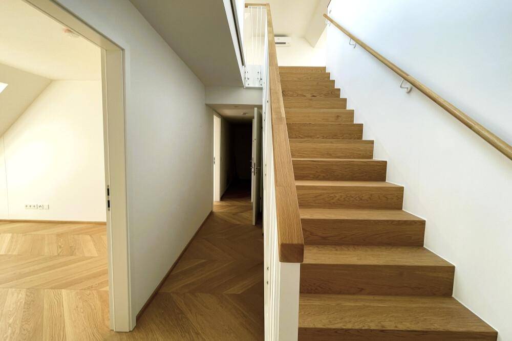Moderner Flur mit Holztreppe und Fischgrätparkett, der zu weiteren Räumen führt.