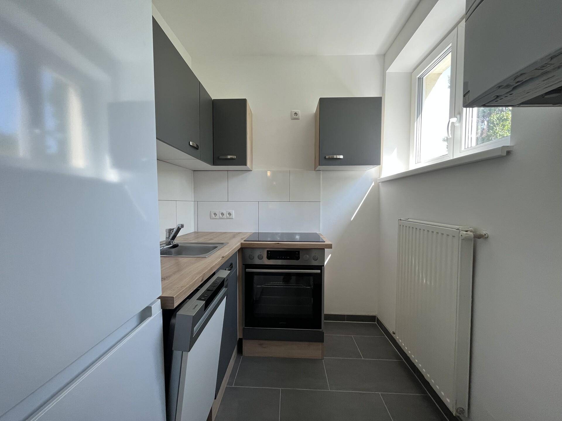 Moderne Einbauküche mit grauen Oberschränken, Holzarbeitsplatte und integrierten Geräten.