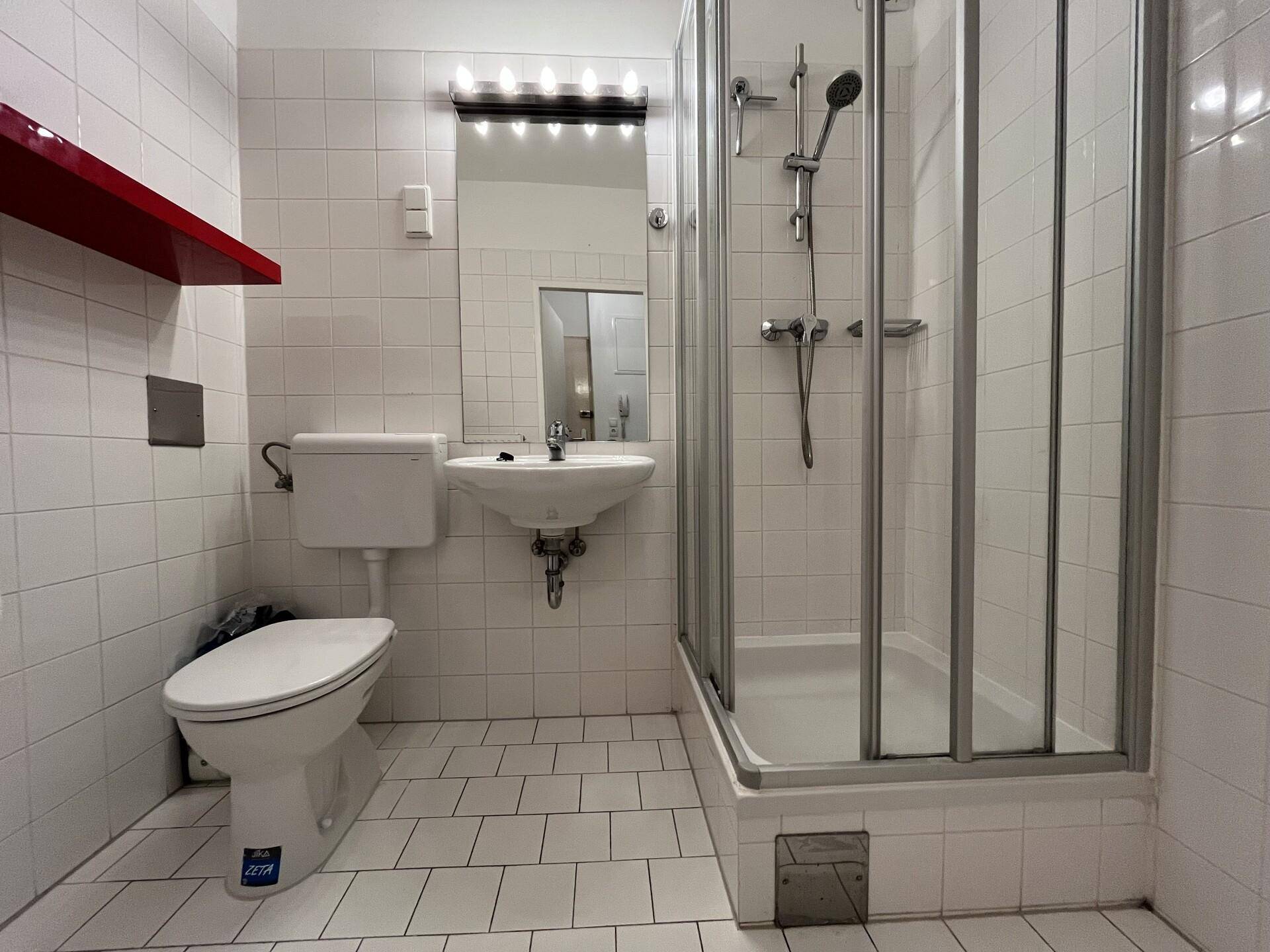 Funktionales Badezimmer mit weiß gefliesten Wänden, Dusche, WC und Waschbecken.