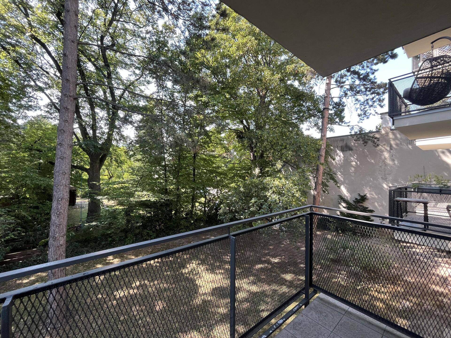 Balkon mit Blick auf üppiges Grün und Bäume, mit einem weiteren Balkon im Hintergrund.