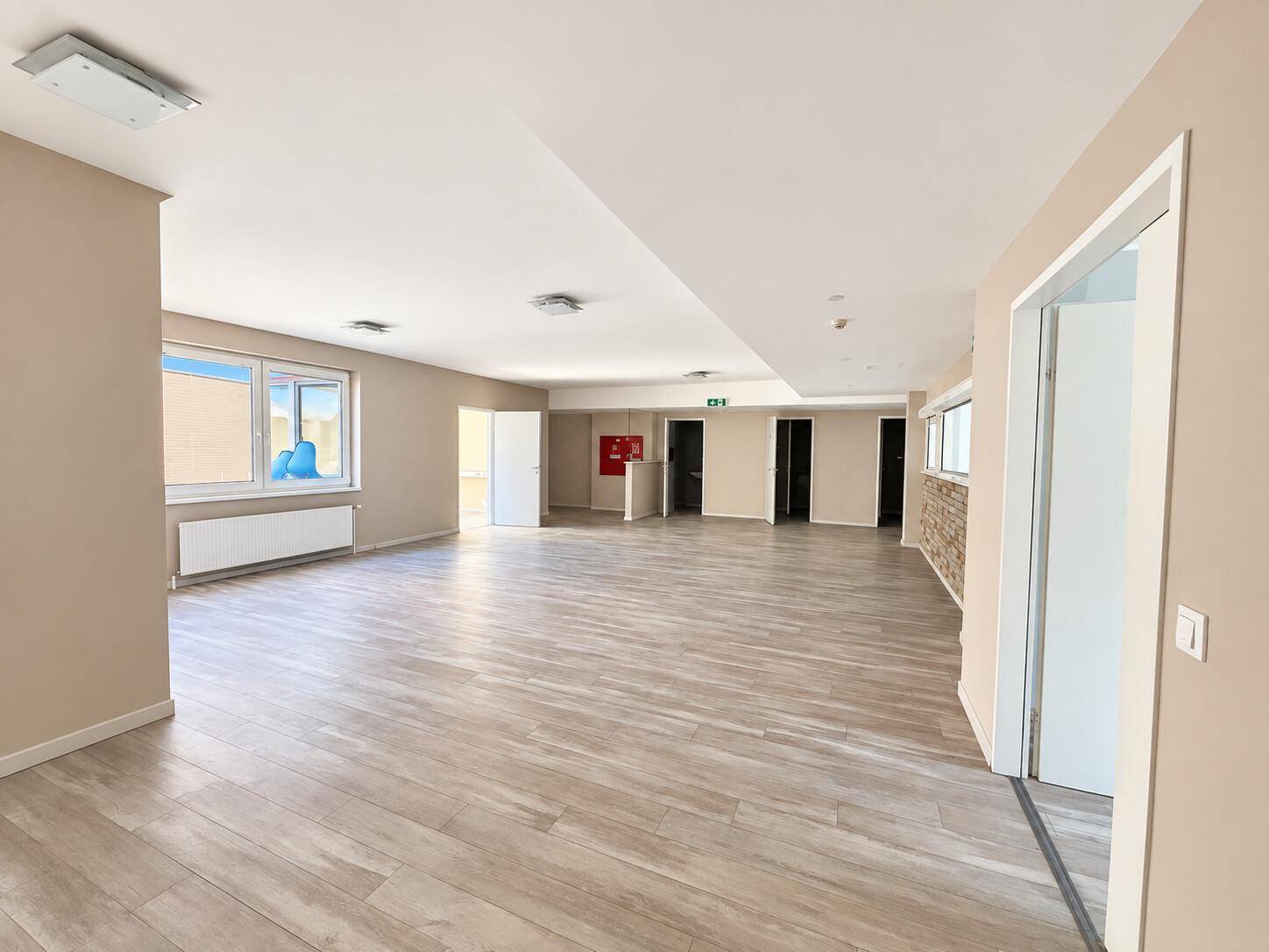Weitläufiger, offener Bürobereich mit Holzoptikboden und mehreren Fenstern, ideal für Großraumbüros.