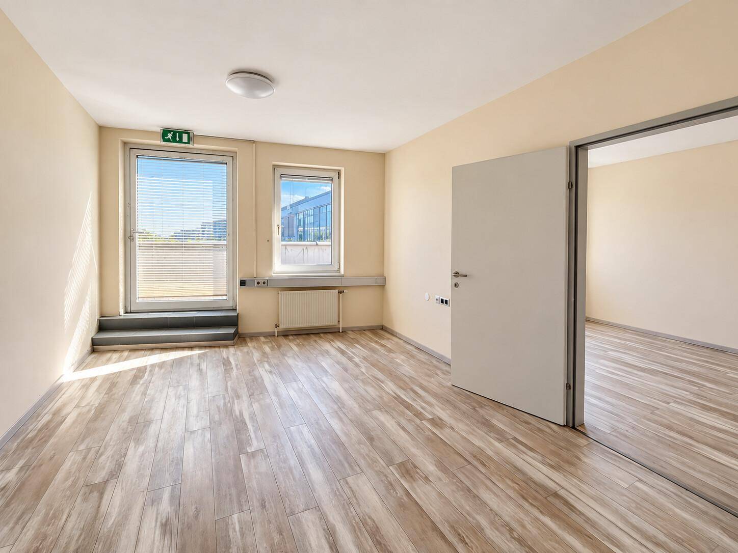 Heller Büroraum mit direktem Zugang nach draußen, einem Fenster und Holzoptikboden.