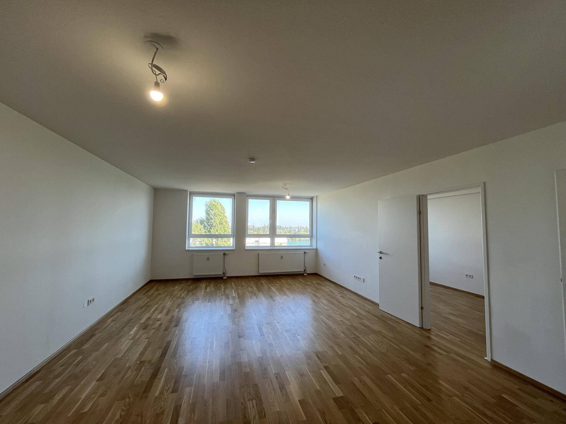 Lichtdurchfluteter Wohnraum mit Holzboden und weitem Blick durch die Fenster.