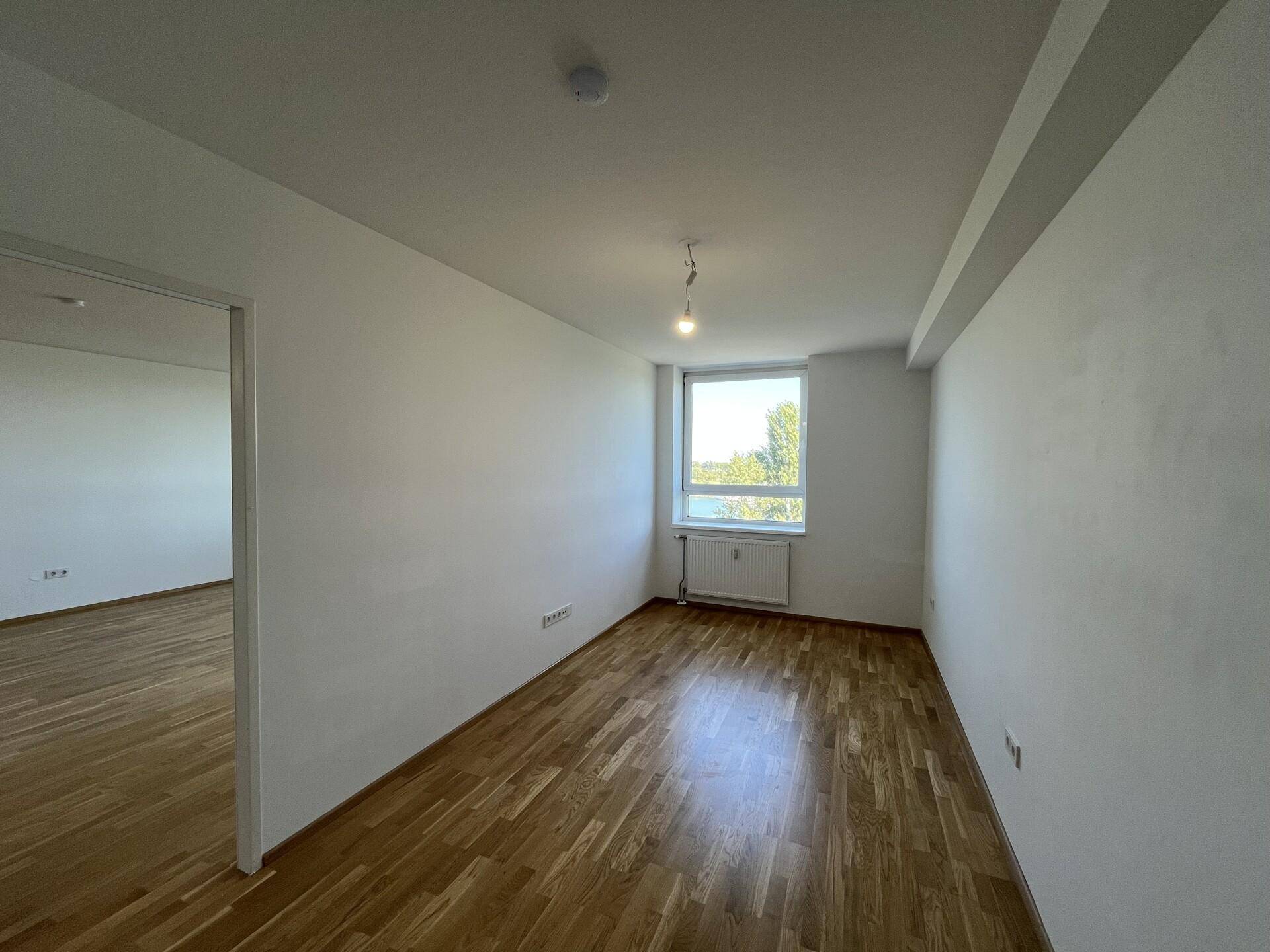 Helles Zimmer mit Holzboden und einem Fenster, ideal als Schlaf- oder Arbeitszimmer.