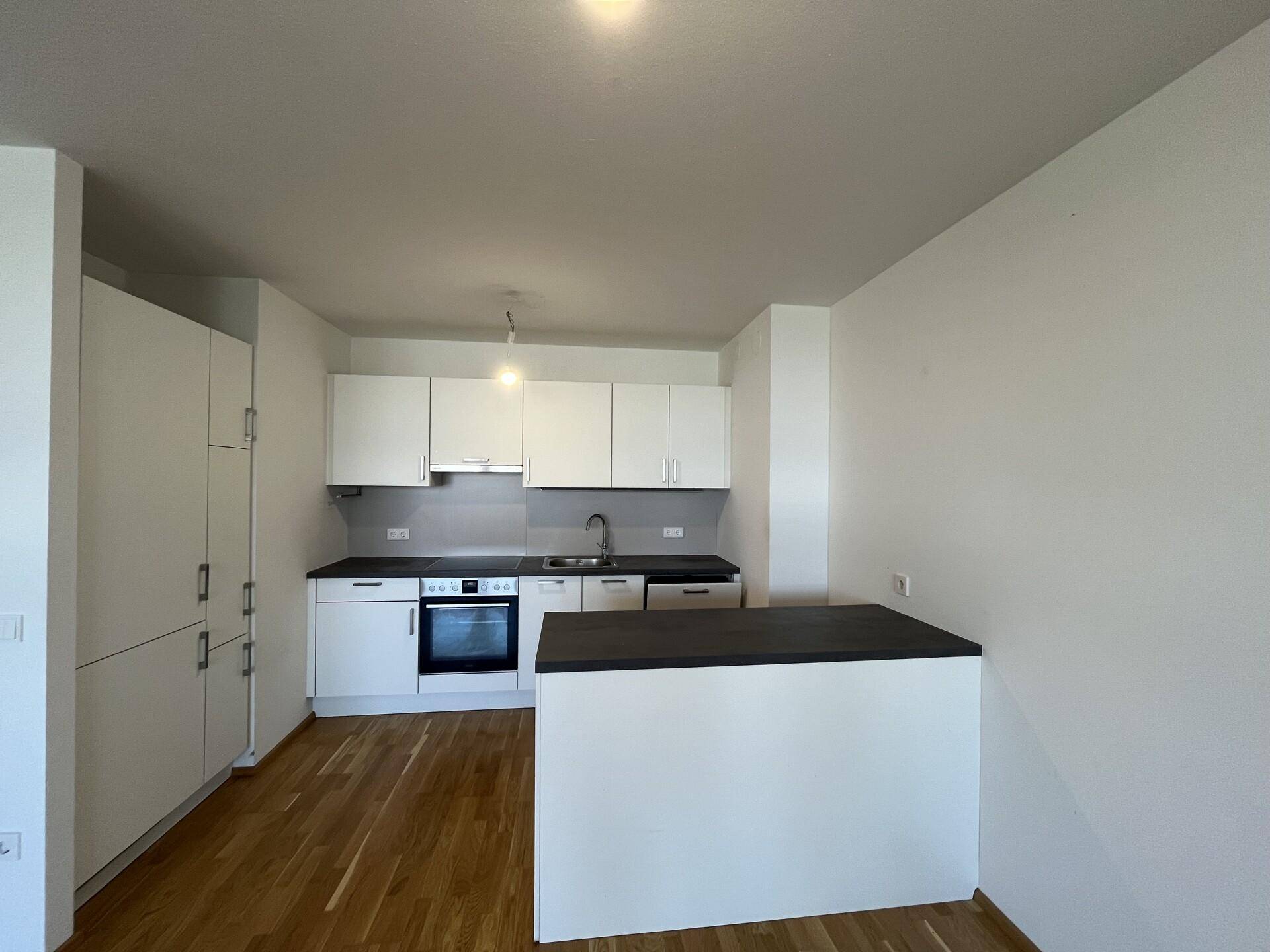 Moderne Einbauküche mit weißen Schränken, dunkler Arbeitsplatte und integriertem Backofen.