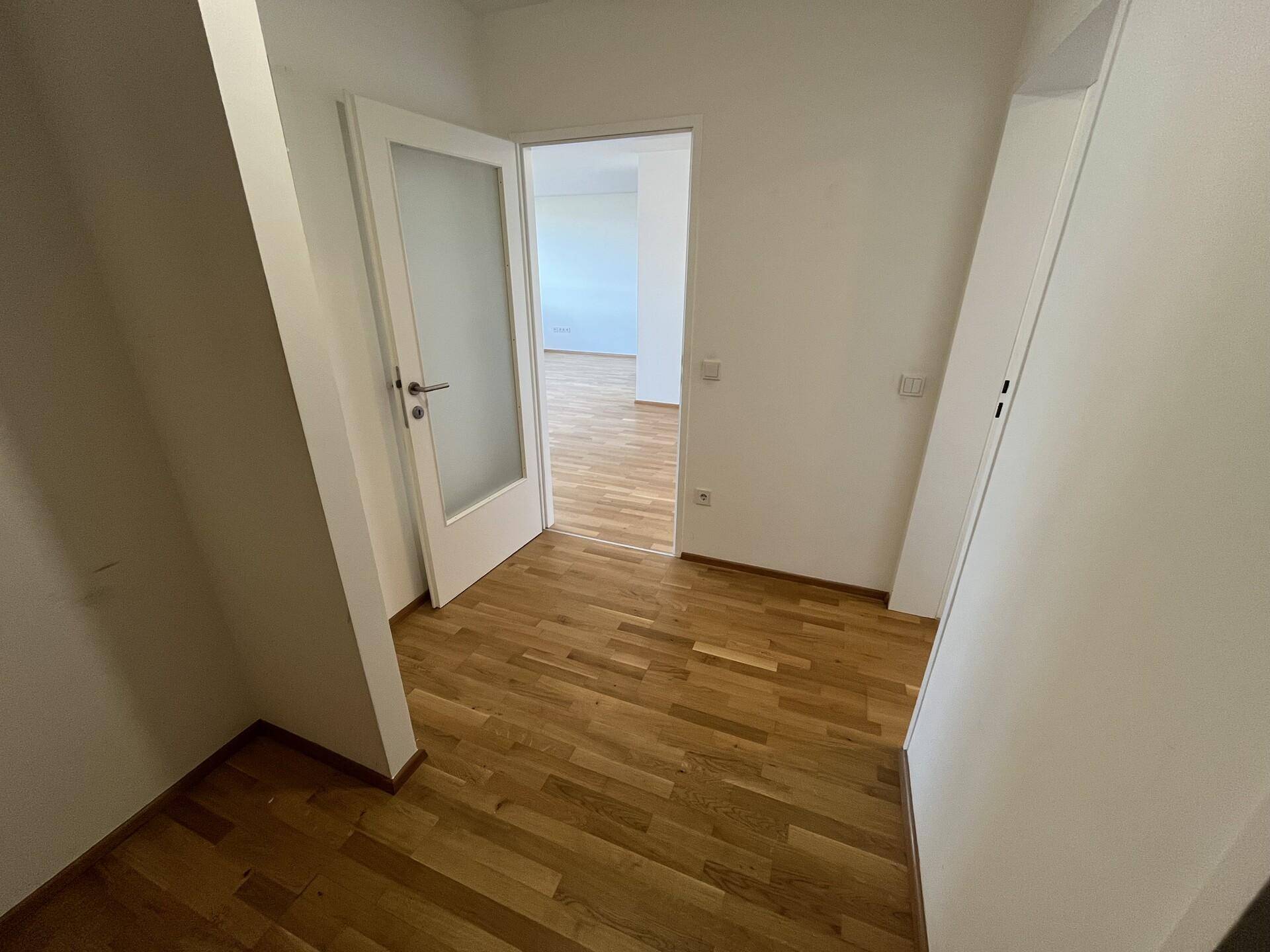 Heller Flur mit Parkettboden und einer Tür, die zu weiteren Räumen der Wohnung führt.