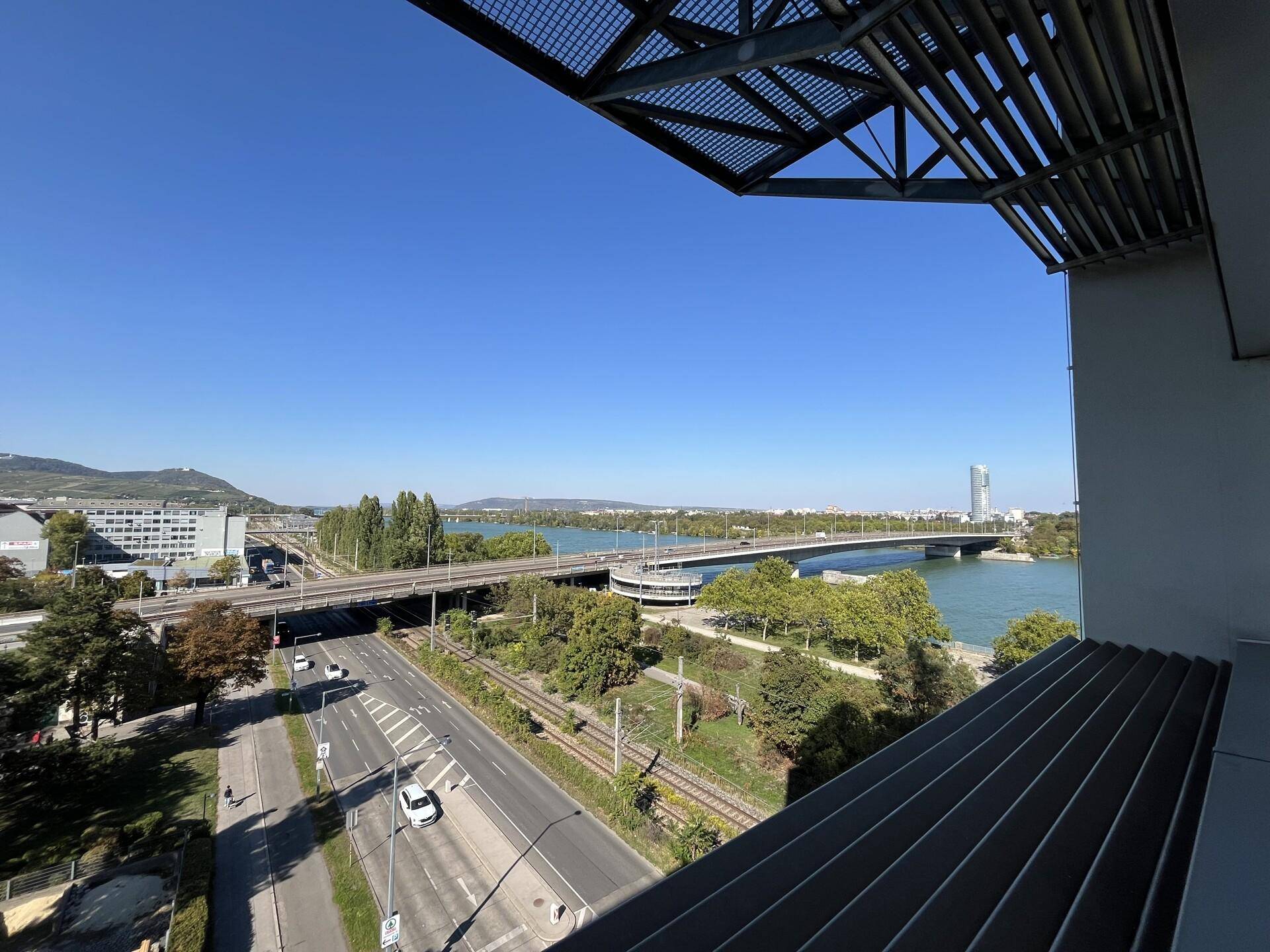 Sonniger Balkon mit weitem Blick auf die Donau, Brücken und die städtische Skyline.