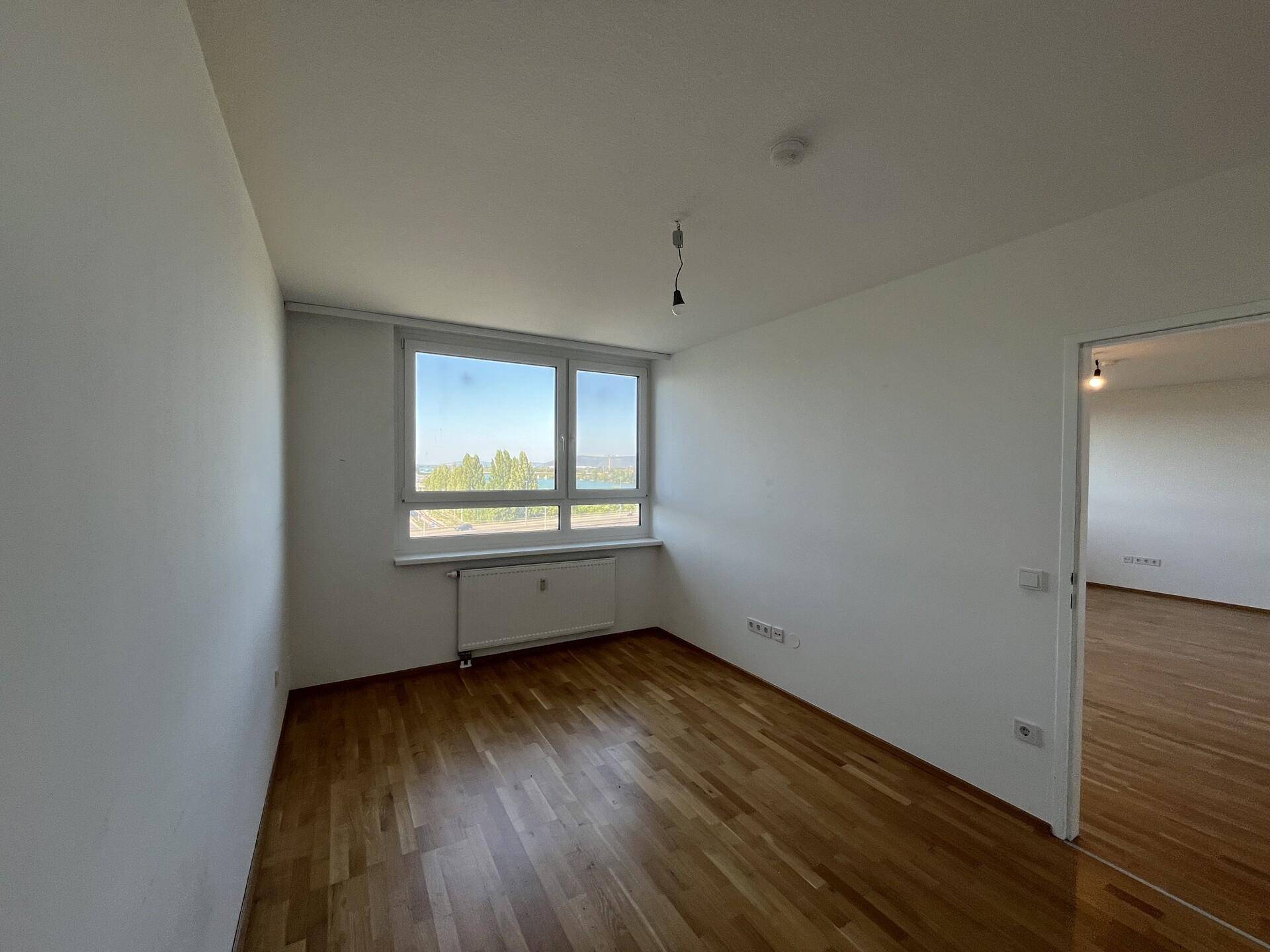 Helles Schlafzimmer mit Parkettboden und Fenster mit Blick auf Wasser und grüne Landschaft.