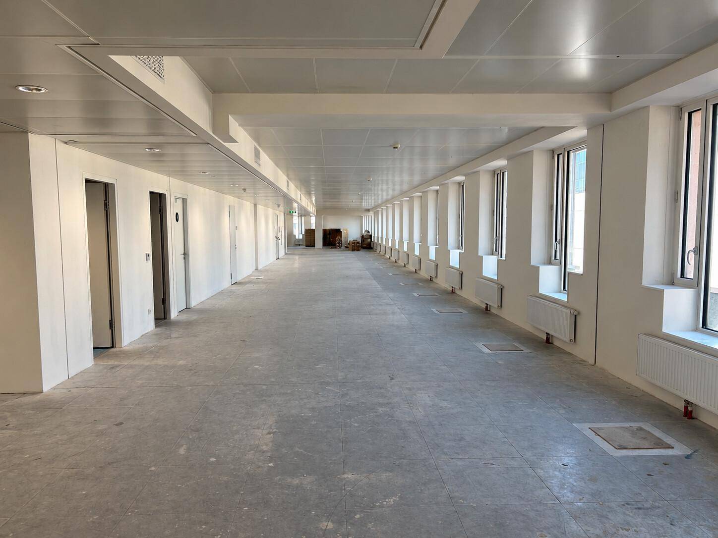Weitläufiger, unmöblierter Bürobereich mit einer Reihe von Fenstern und einem schlichten Decken- und Bodendesign.