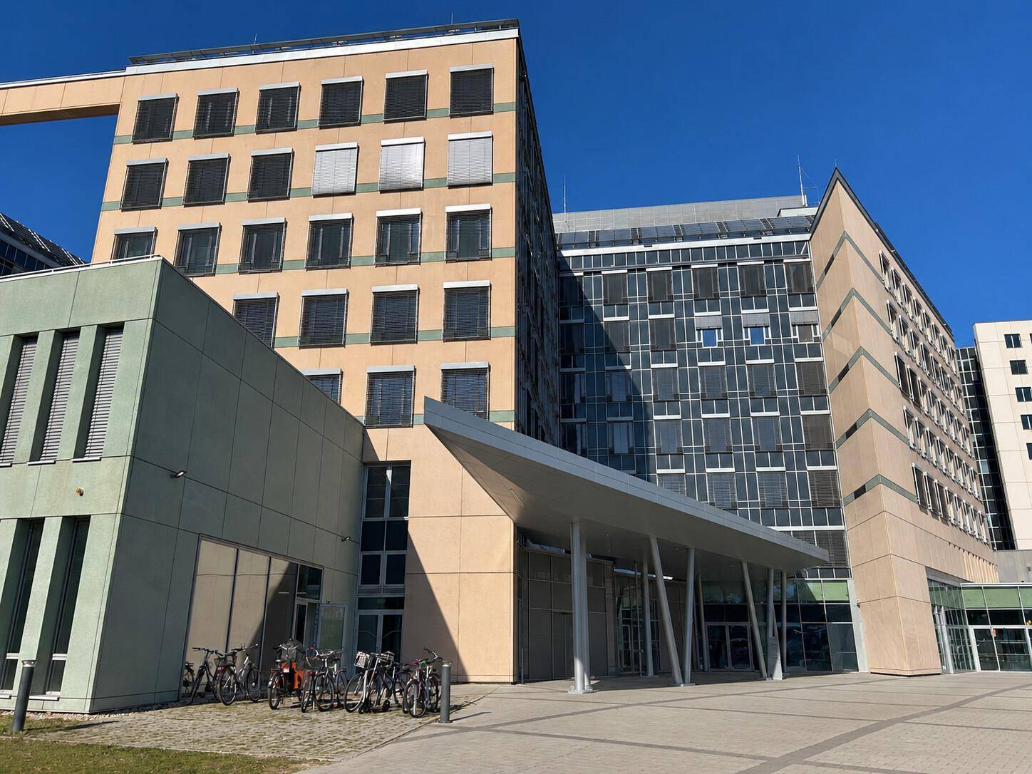 Moderne Bürogebäude mit unterschiedlichen Fassadenmaterialien und einem großzügigen Eingangsbereich im Freien.