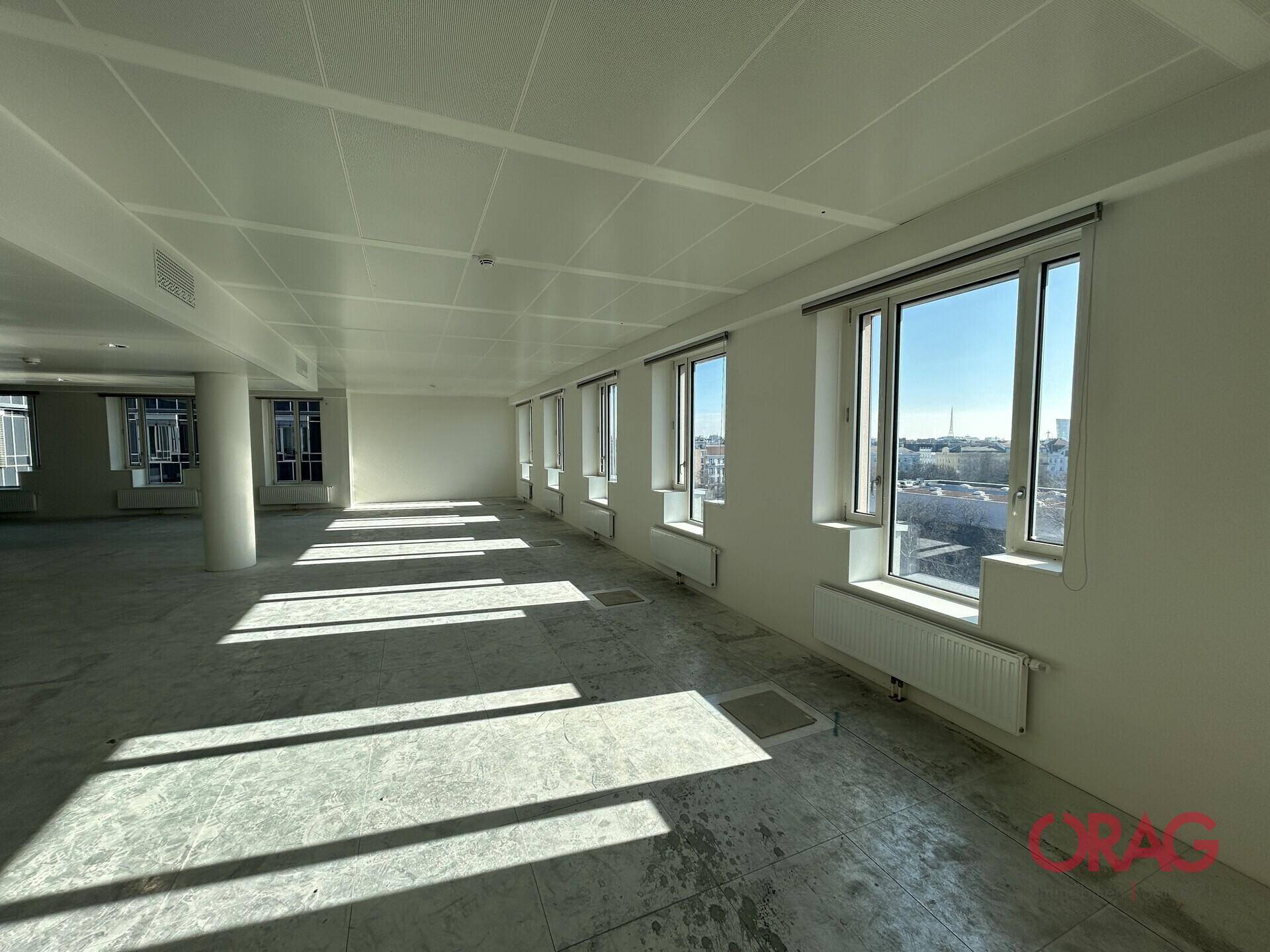 Geräumiger, leerer Büroraum mit vielen Fenstern, die viel Tageslicht hereinlassen und eine weite Aussicht bieten.