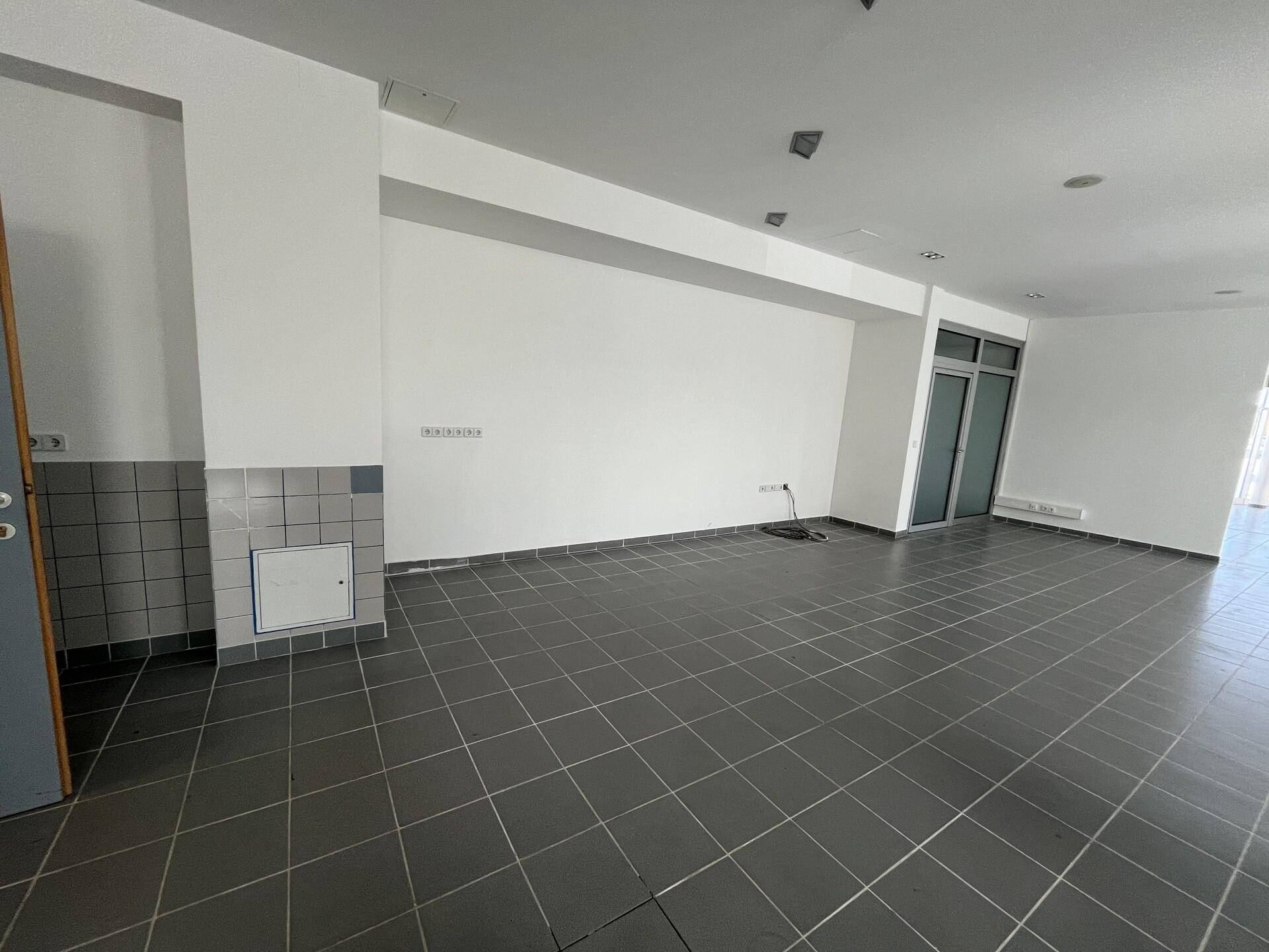 Weiterer Blick in den großen Gewerberaum mit grauen Fliesen und einer gefliesten Wandpartie.